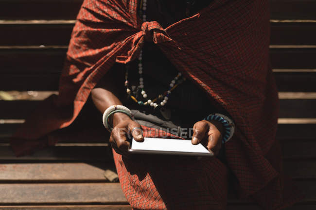 Масаї людина в традиційному одязі, використовуючи цифровий планшет на лавці — стокове фото