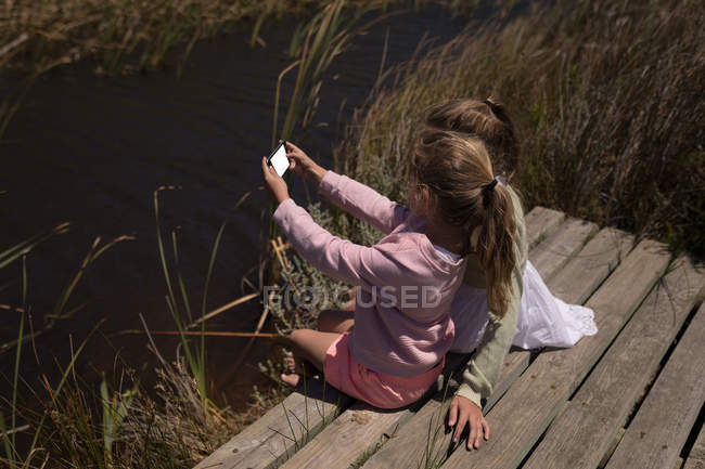 Siblings taking selfie with mobile phone on jetty — Stock Photo