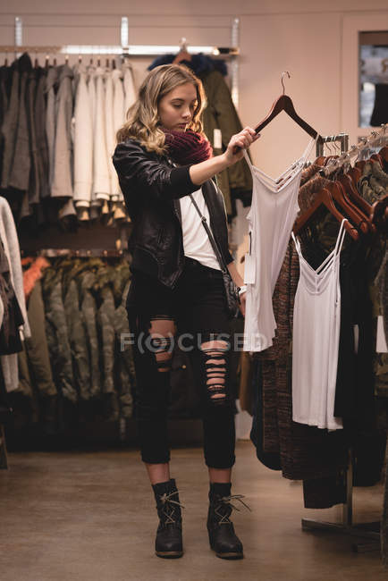 Beautiful girl selecting clothes from rack in shopping mall — Stock Photo