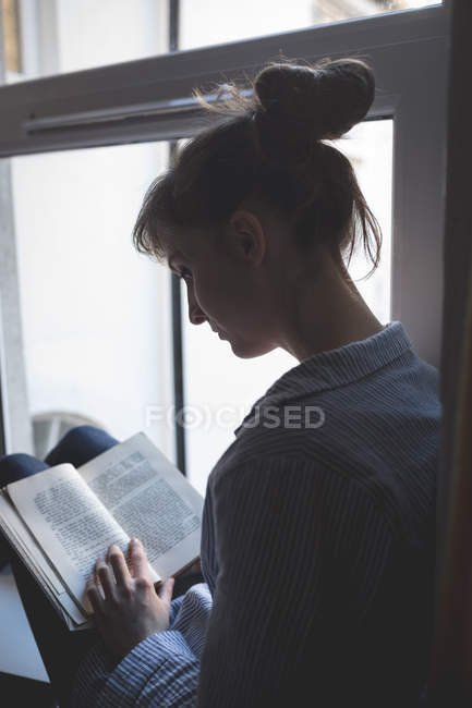 Frau liest Buch am Fenster zu Hause — Stockfoto