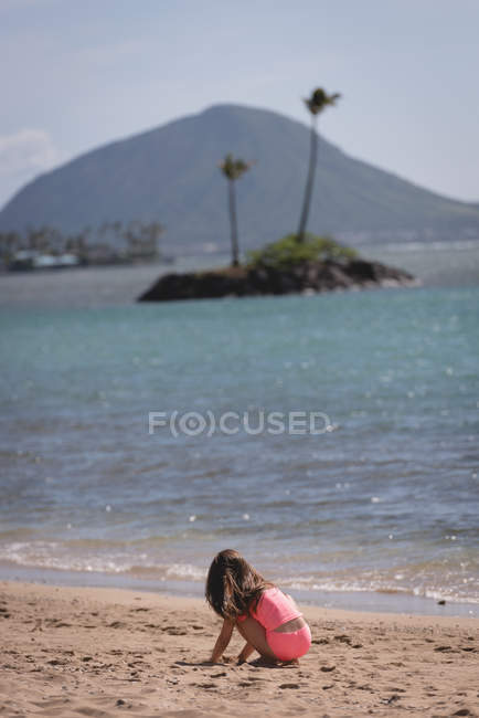 Seitenansicht eines Mädchens im Grundschulalter, das im Sand am Strand spielt — Stockfoto
