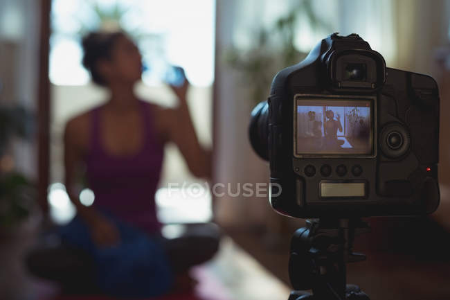 Primer plano de la grabación de la cámara video blogger femenina bebiendo agua en casa - foto de stock