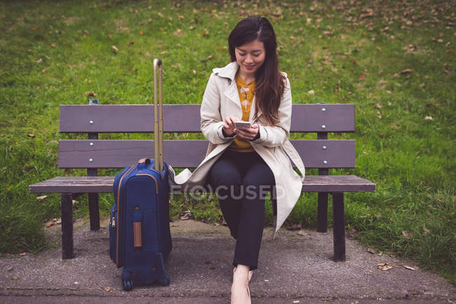Donna d'affari sorridente utilizzando il telefono cellulare mentre seduto sulla panchina — Foto stock