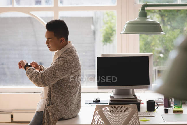Executive sitting on desk checking time in his smartwatch in the office — Stock Photo