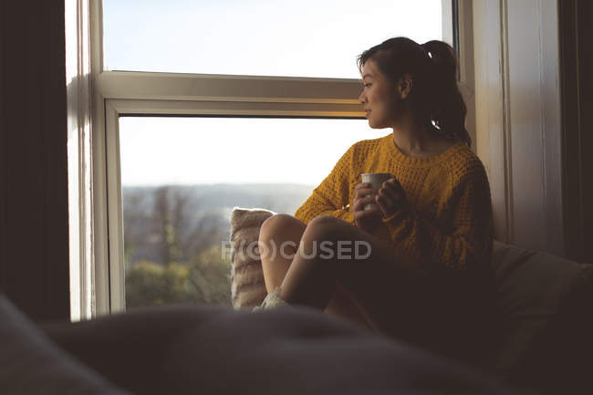 Femme réfléchie prenant un café près de la fenêtre à la maison — Photo de stock