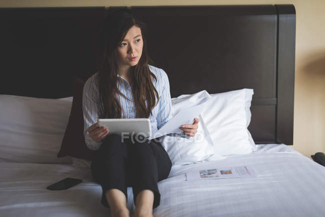 Бізнес-леді тримає документи під час використання цифрового планшета на ліжку в готельному номері — стокове фото