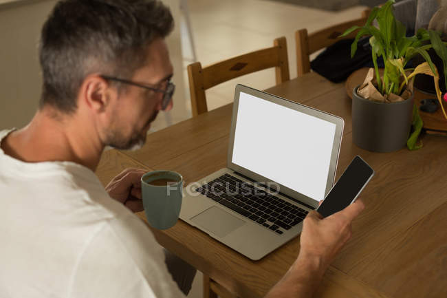 Чоловік має каву під час використання мобільного телефону вдома — стокове фото
