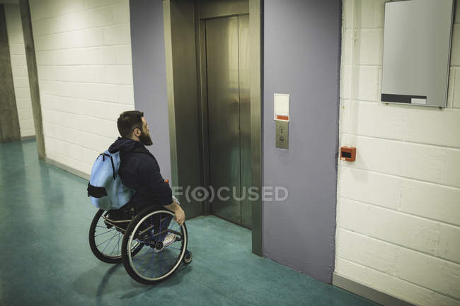 Handicapped man with backpack on wheelchair waiting for elevator indoors — Stock Photo