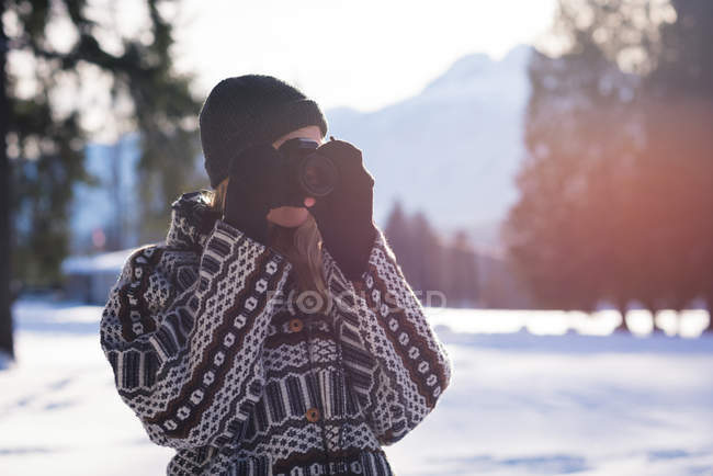 Mulher fotografando com câmera na neve em um dia ensolarado — Fotografia de Stock