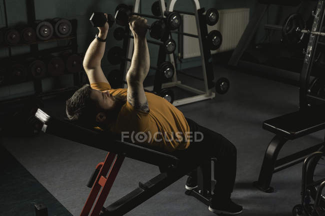 Людина з інвалідністю піднімає гантелі на лавці в спортзалі — стокове фото