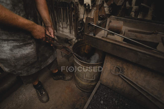 Кузнец погружает в воду раскаленный металлический стержень в мастерской — стоковое фото