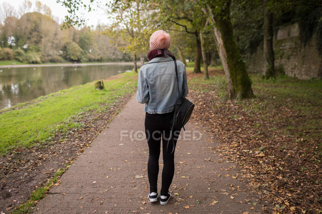 Vue arrière de la jeune femme en vêtements chauds debout dans le parc avec sac à dos — Photo de stock