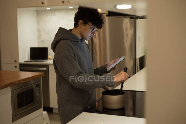 Mulher bonita usando tablet digital enquanto cozinha comida na cozinha — Fotografia de Stock