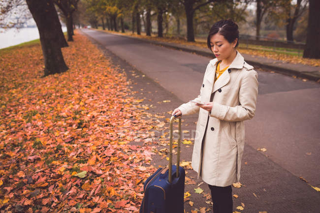 Businesswoman using mobile phone in street during autumn — Stock Photo