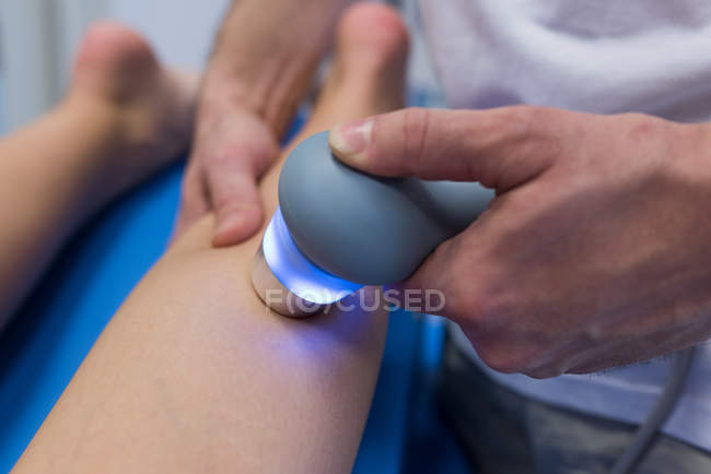 Physiotherapist giving leg massage to woman with machine in clinic — Stock Photo