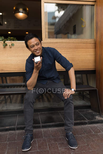 Hombre de negocios sonriente hablando por teléfono en la cafetería del pavimento - foto de stock