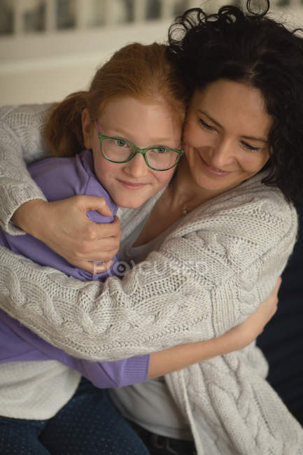 Madre e hija abrazándose en la sala de estar en casa - foto de stock