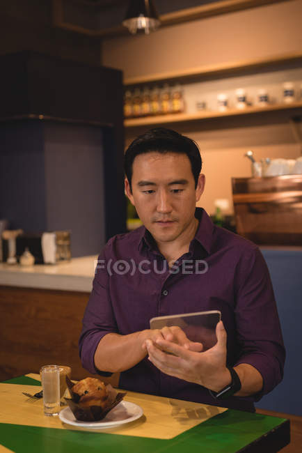 Hombre asiático usando tableta digital mientras está sentado en la cafetería - foto de stock