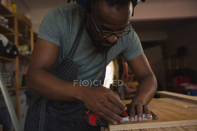 Плотник измеряет деревянную доску с рулеткой в мастерской — стоковое фото
