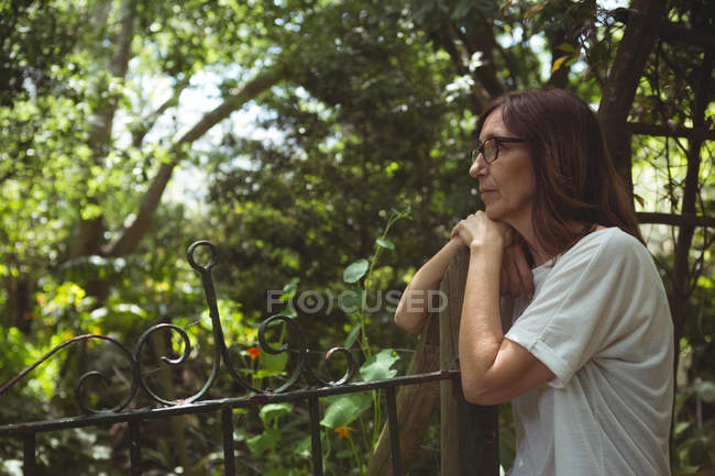 Nachdenkliche Frau lehnt an Tor im Garten — Stockfoto