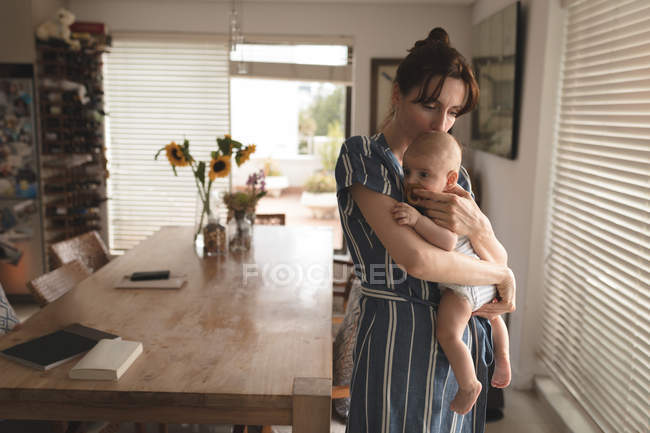 Jovem mãe no banho roubar segurando e beijando seu bebê na sala de estar em casa — Fotografia de Stock