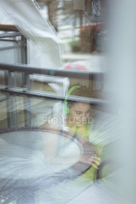 Молодая женщина лежит на кровати в наушниках, используя свой ноутбук дома — стоковое фото