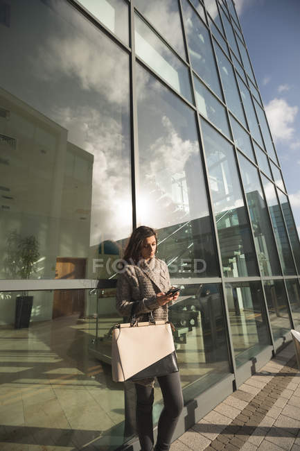 Молода жінка використовує смартфон за межами сучасної будівлі — стокове фото