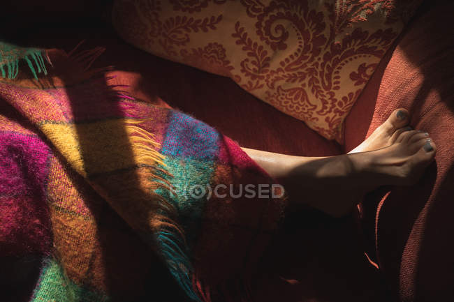 Жінка ноги покриті барвистою ковдрою на ліжку вдома — стокове фото