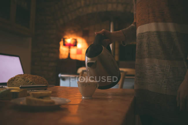 Partie médiane de la femme versant de l'eau chaude dans une tasse à la maison — Photo de stock