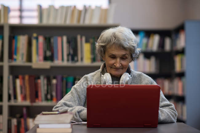 Active senior woman using laptop in library — Stock Photo