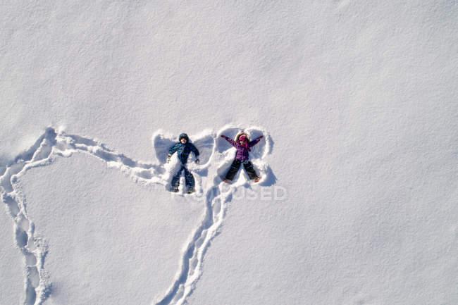 Дети, лежащие на снегу и создающие форму снежного ангела — стоковое фото