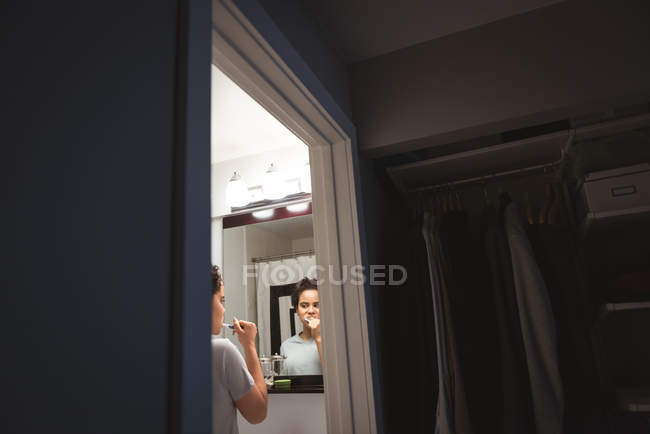 Young woman standing in front of mirror brushing her teeth in the bathroom at home — Stock Photo