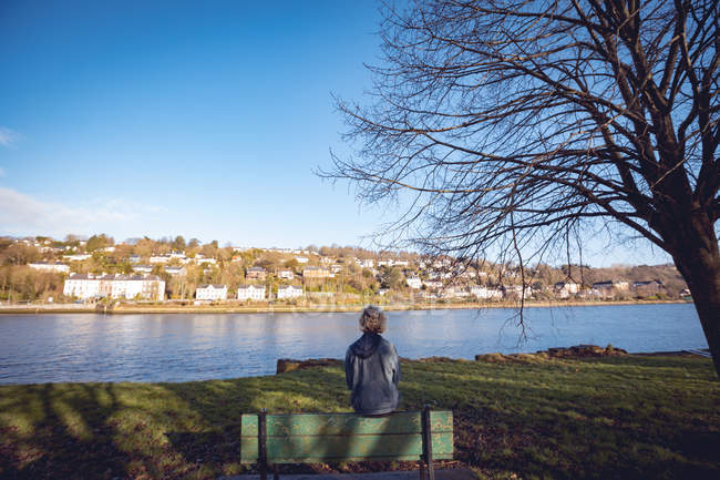 Vue arrière d'une femme assise sur un banc près d'une rivière — Photo de stock