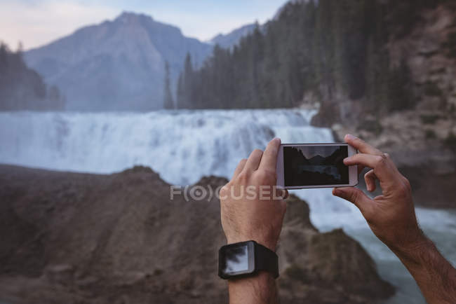 Close-up of man taking photo of waterfall with mobile phone — Stock Photo