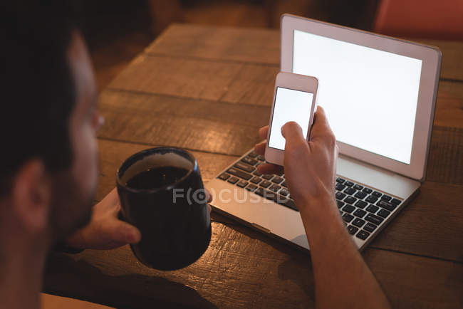 Крупним планом вид людини, що використовує мобільний телефон, тримаючи каву в кафе . — стокове фото