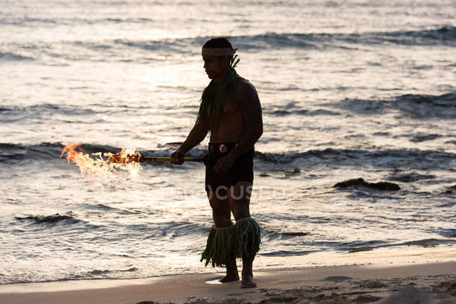 Male fire dancer performing with fire levi stick at beach — Stock Photo