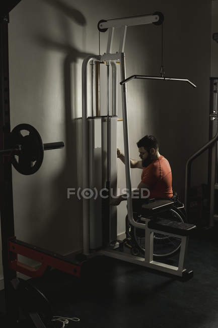 Handicapped man on wheelchair increasing weight of pulldown exercise in gym — Stock Photo