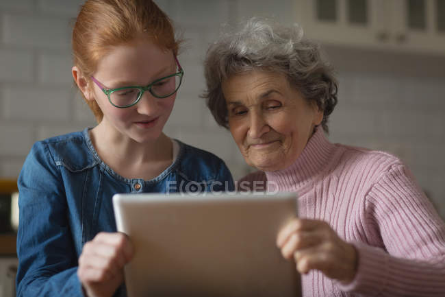 Avó e neta usando tablet digital na cozinha em casa — Fotografia de Stock