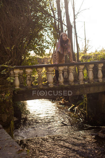 Продумана жінка спирається на пішохідний міст у лісі — стокове фото