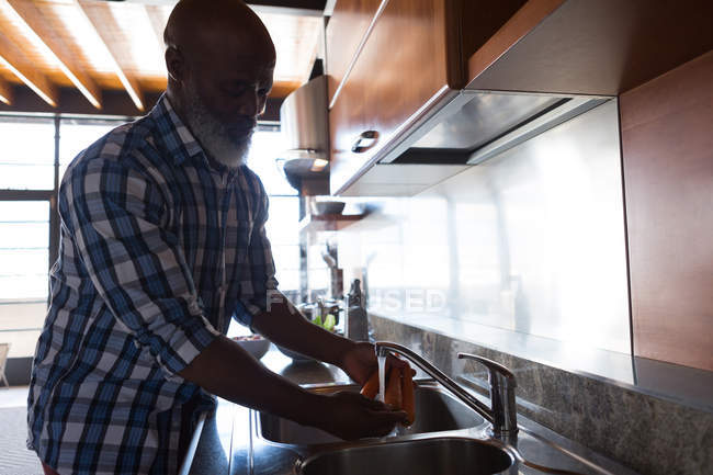 Старший чоловік миє моркву на кухні в раковині вдома — стокове фото