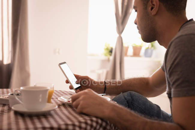 Мужчина пользуется мобильным телефоном во время завтрака на кухне дома . — стоковое фото