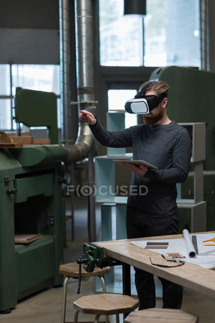 Carpinteiro masculino com tablet digital usando fone de ouvido realidade virtual na oficina — Fotografia de Stock