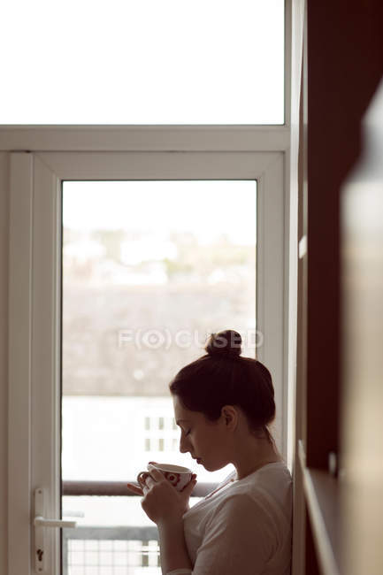 Junge Frau riecht Kaffee und lehnt sich zu Hause an Wand. — Stockfoto