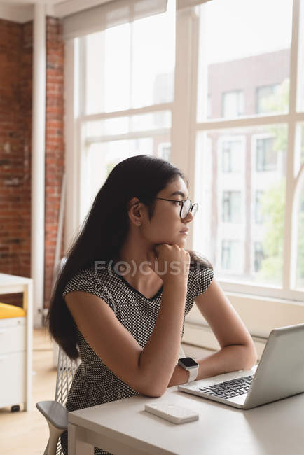 Exécutif féminin réfléchi regardant par la fenêtre dans le bureau créatif — Photo de stock