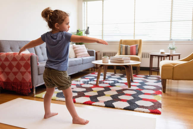 Маленькая девочка выполняет упражнения на растяжку в гостиной на дому — стоковое фото