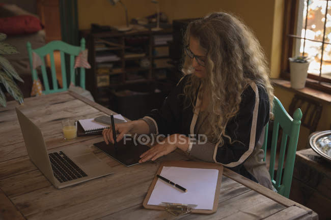 Зріла жінка сидить на стільці і використовує свій планшет вдома — стокове фото