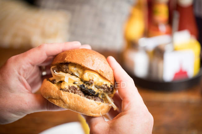 Gros plan des mains masculines tenant un hamburger au restaurant . — Photo de stock