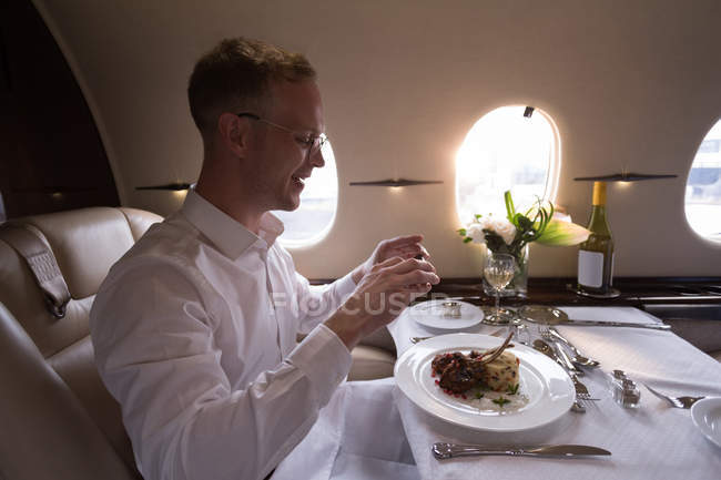 Empresário tira foto de refeição com celular em jato particular — Fotografia de Stock