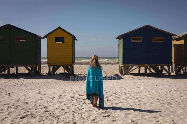 Vue arrière de la fille debout enveloppée dans une couverture debout sur la plage — Photo de stock