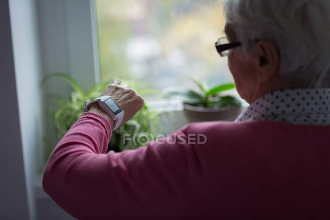 Donna anziana controllare il tempo sul suo orologio a casa — Foto stock